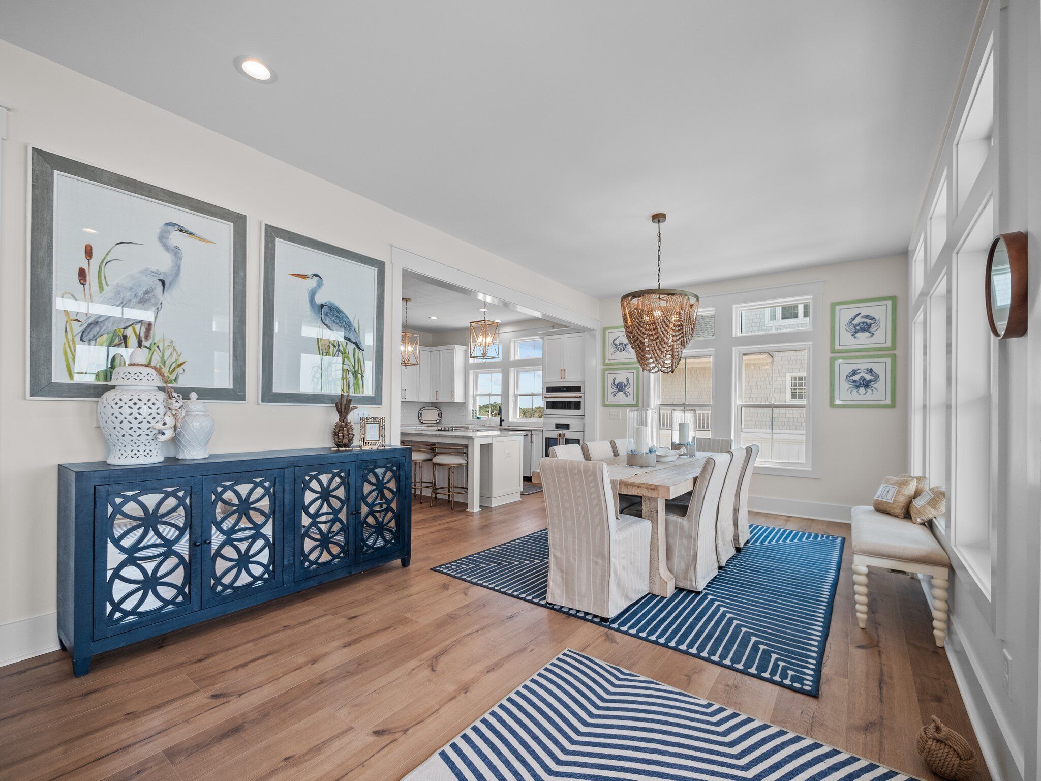 A spacious kitchen with white cabinets, a wooden dining table, and blue-striped rugs.