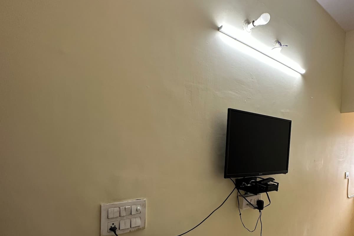 A room with a mounted TV, a light strip above it, and a power outlet on the wall.