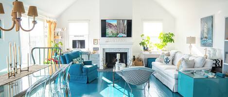 A spacious living room with a high ceiling, a fireplace, and a large TV mounted above it.