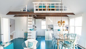Un vaste espace de vie doté d’un haut plafond, une table à manger avec des chaises, un coin cuisine et un escalier menant à une chambre en mezzanine.