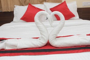 A bed with white bedding and red pillows, and two white towels arranged in a heart shape. - Sanjiva Suites (Barasat)