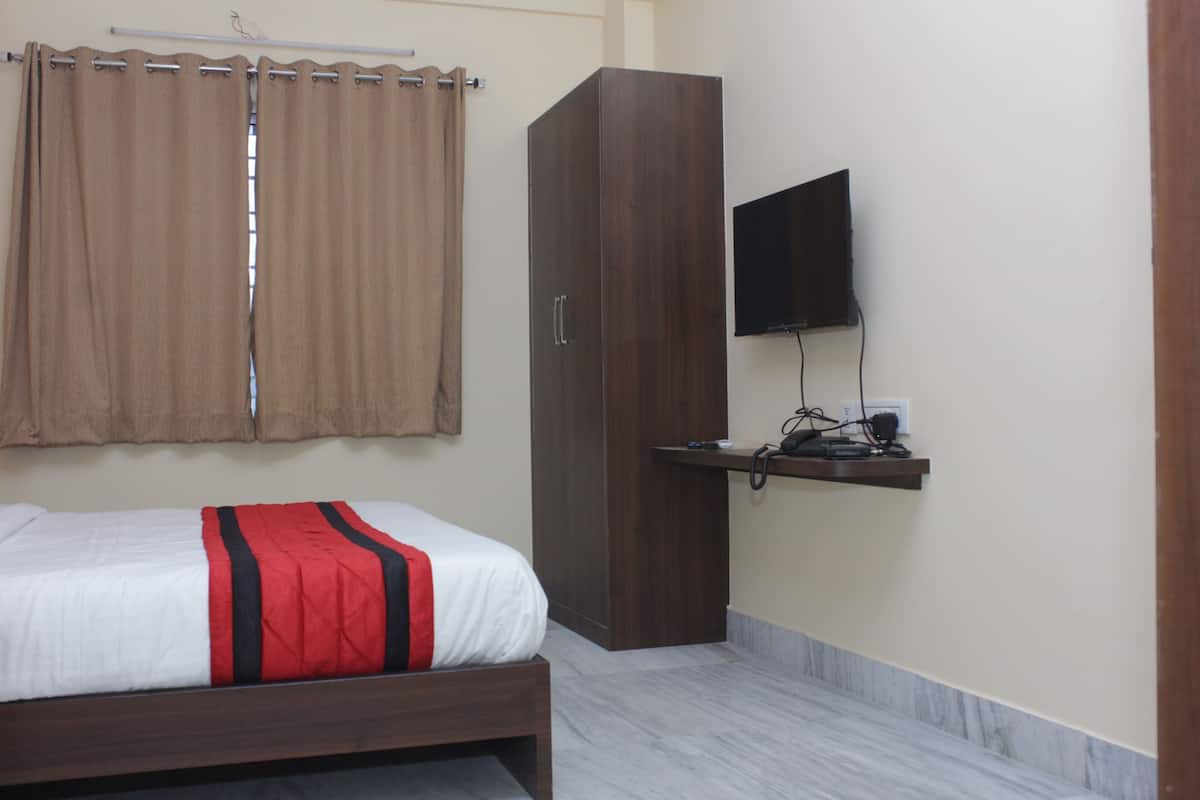 A bedroom with a bed, a wardrobe, a television mounted on the wall, and a small shelf with electronic devices.