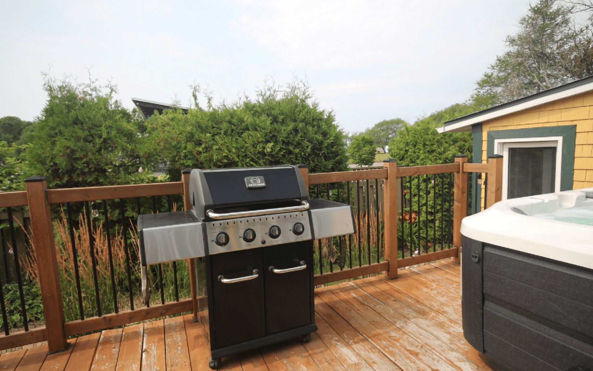 A barbecue grill on a wooden deck with a hot tub nearby.
