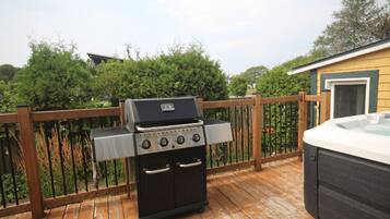A barbecue grill on a wooden deck with a hot tub nearby.