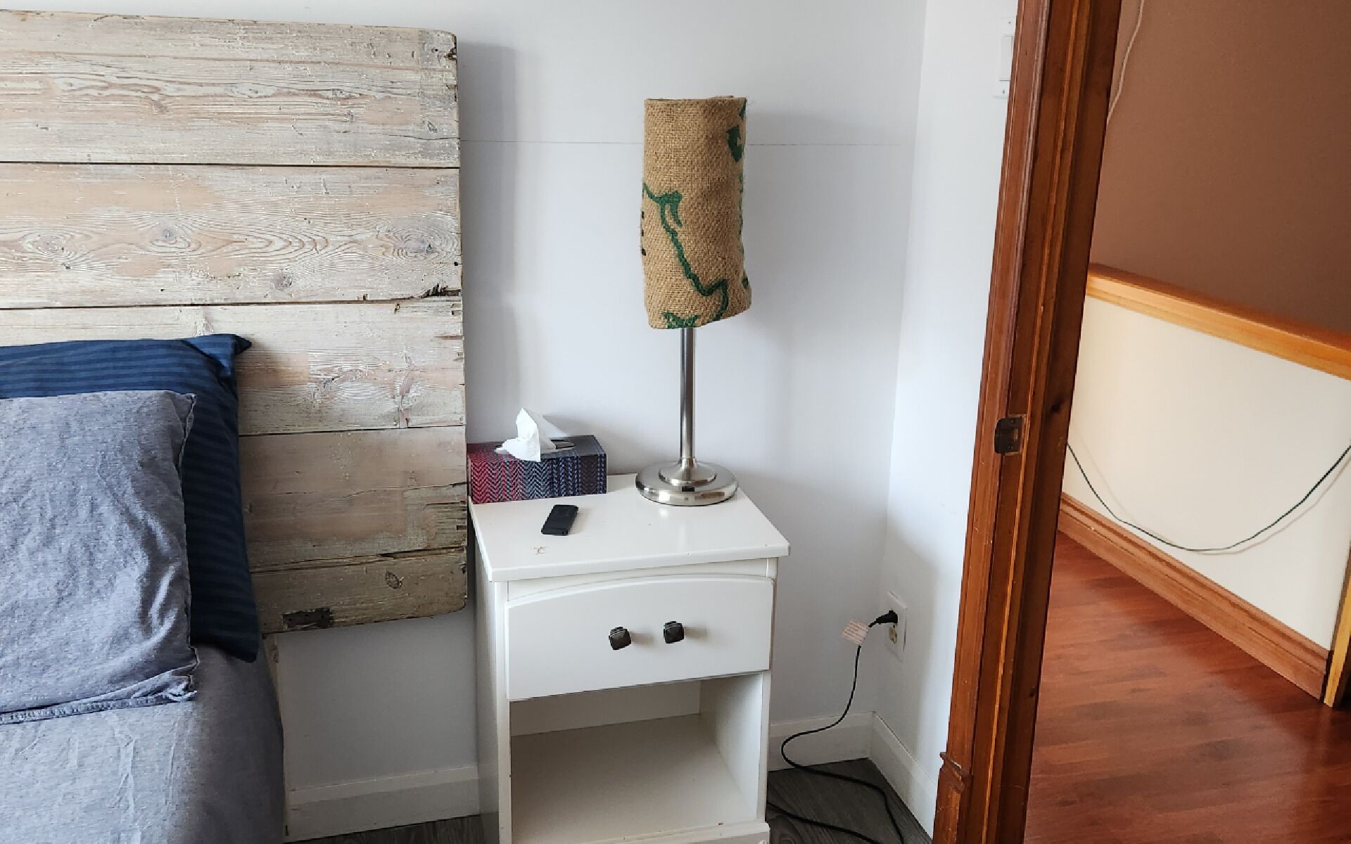 Une petite table de chevet blanche, avec une lampe, une boîte de mouchoirs et une télécommande.