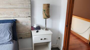 A small white bedside table with a lamp, a tissue box, and a remote control.