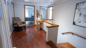 A spacious room with hardwood flooring, a wooden chair, a small table with a vase and plant, a staircase with a wooden handrail, and a large abstract painting on the wall. - Distinctive 5-room inn, located a few steps from the river to discover the multi (SAINT JEAN PORT JOLI)
