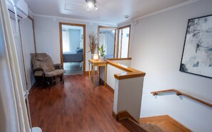 A spacious room with hardwood flooring, a wooden chair, a small table with a vase and plant, a staircase with a wooden handrail, and a large abstract painting on the wall. - Distinctive 5-room inn, located a few steps from the river to discover the multi (SAINT JEAN PORT JOLI)