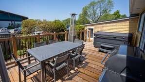 Une terrasse en bois avec une table et des chaises, un barbecue et un espace salon abrité.