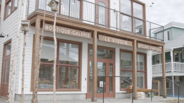 Un bâtiment dont les devantures de magasins portent les inscriptions « BOUTIQUE-GALERIE » et « LE VIVOIR ».