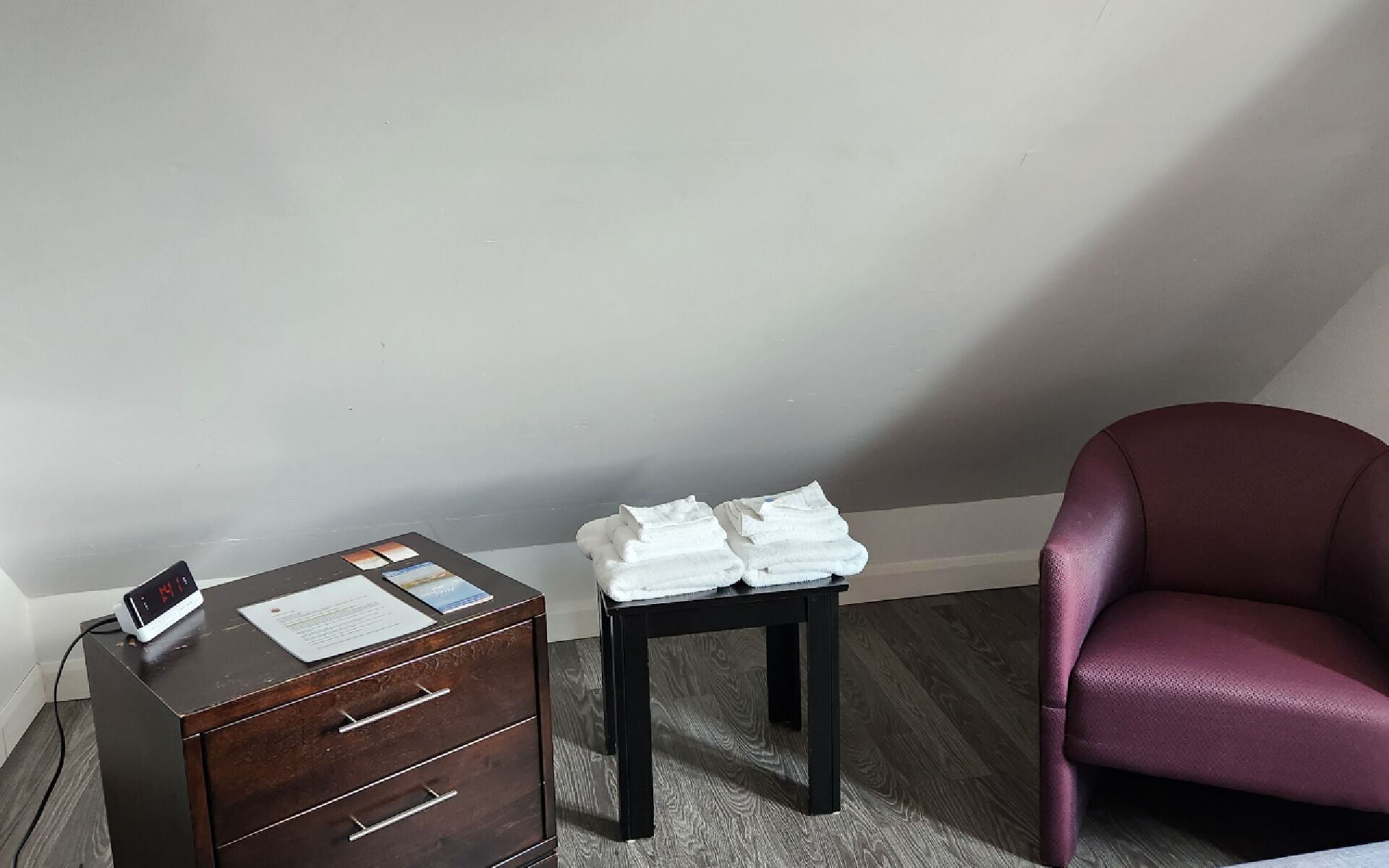 A room with a wooden desk, a small table with folded towels, and a purple chair.