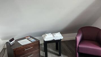 A room with a wooden desk, a small table with folded towels, and a purple chair.