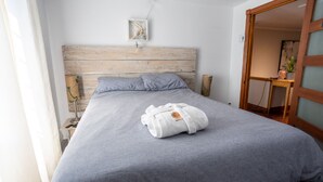 Un lit bien fait, recouvert d’une couverture grise, avec deux oreillers et un peignoir blanc posé dessus.