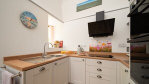 A modern kitchen with a wooden countertop, white cabinets, a stainless steel sink, and a black range hood.