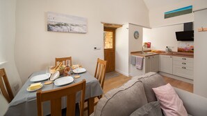 A cozy dining area with a table set for two, a wooden door leading to a kitchen, and a painting on the wall.