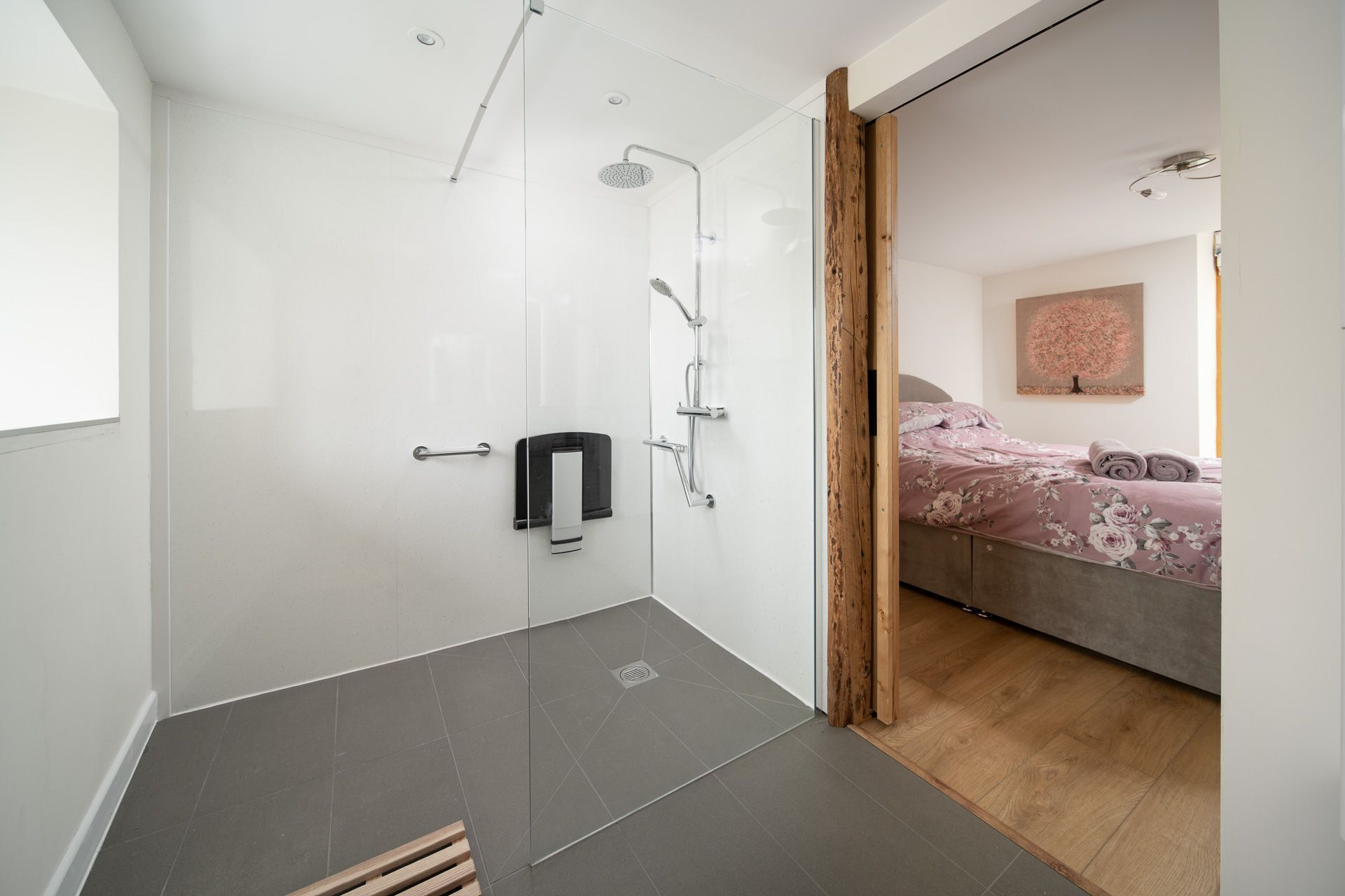 Un baño moderno con cabina de ducha de vidrio, un perchero y suelo de madera.