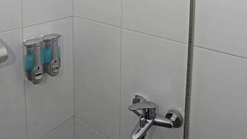 Een douchegedeelte met een handdouche en een kraan op de muur.