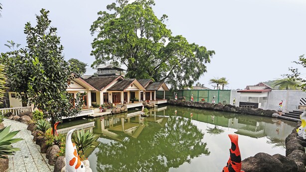 Ein friedlicher Hotelinnenhof mit einem Teich, in dem sich das Licht spiegelt, traditionellen Gebäuden und einem gepflegten Garten.