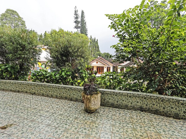 Un patio con baldosas y una jardinera de piedra, rodeado de abundante vegetación y un muro de piedra.