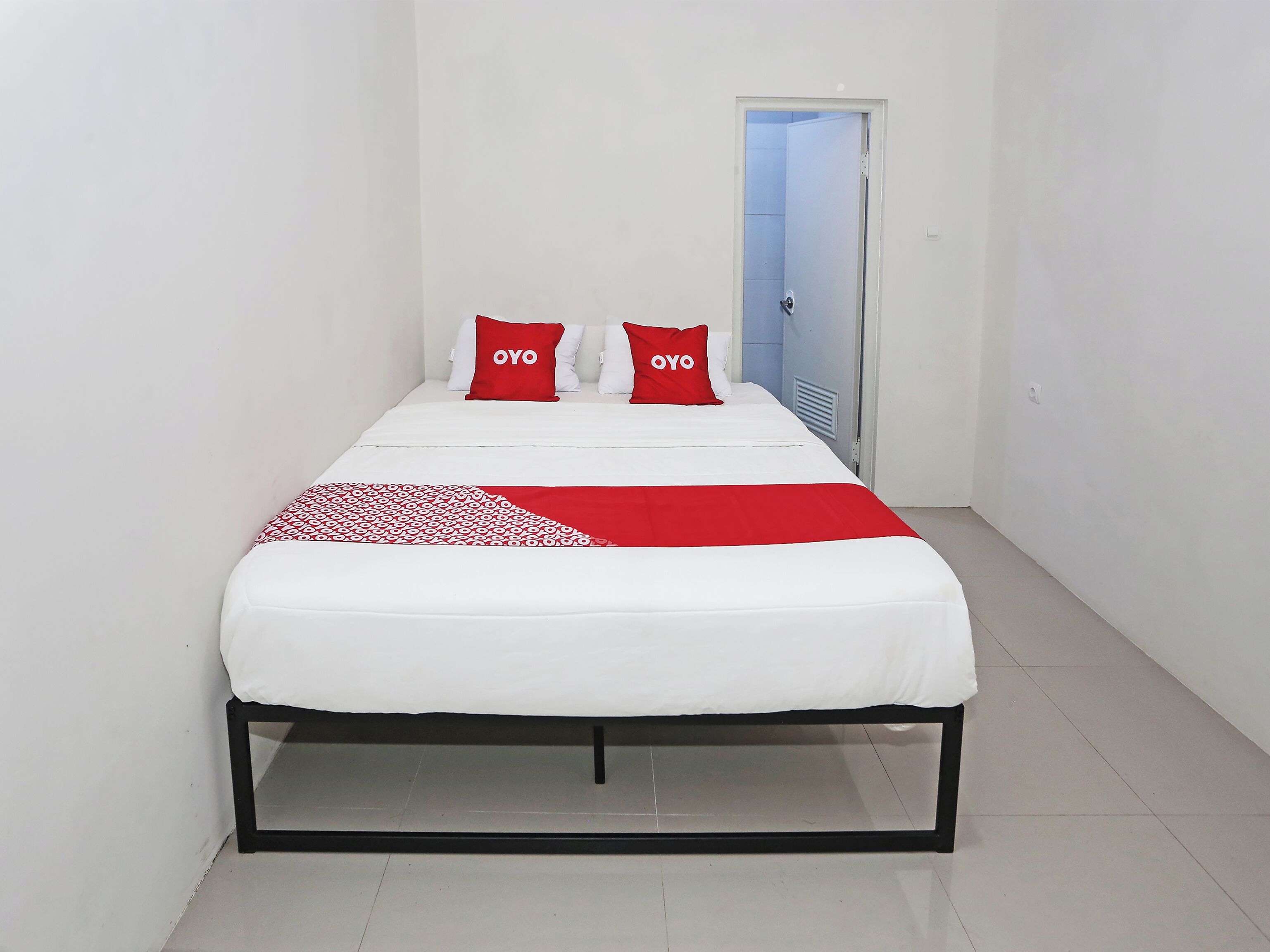 A single-bed room with a white bedspread, two red pillows with the word "OYO" on them, and a red and white patterned throw.