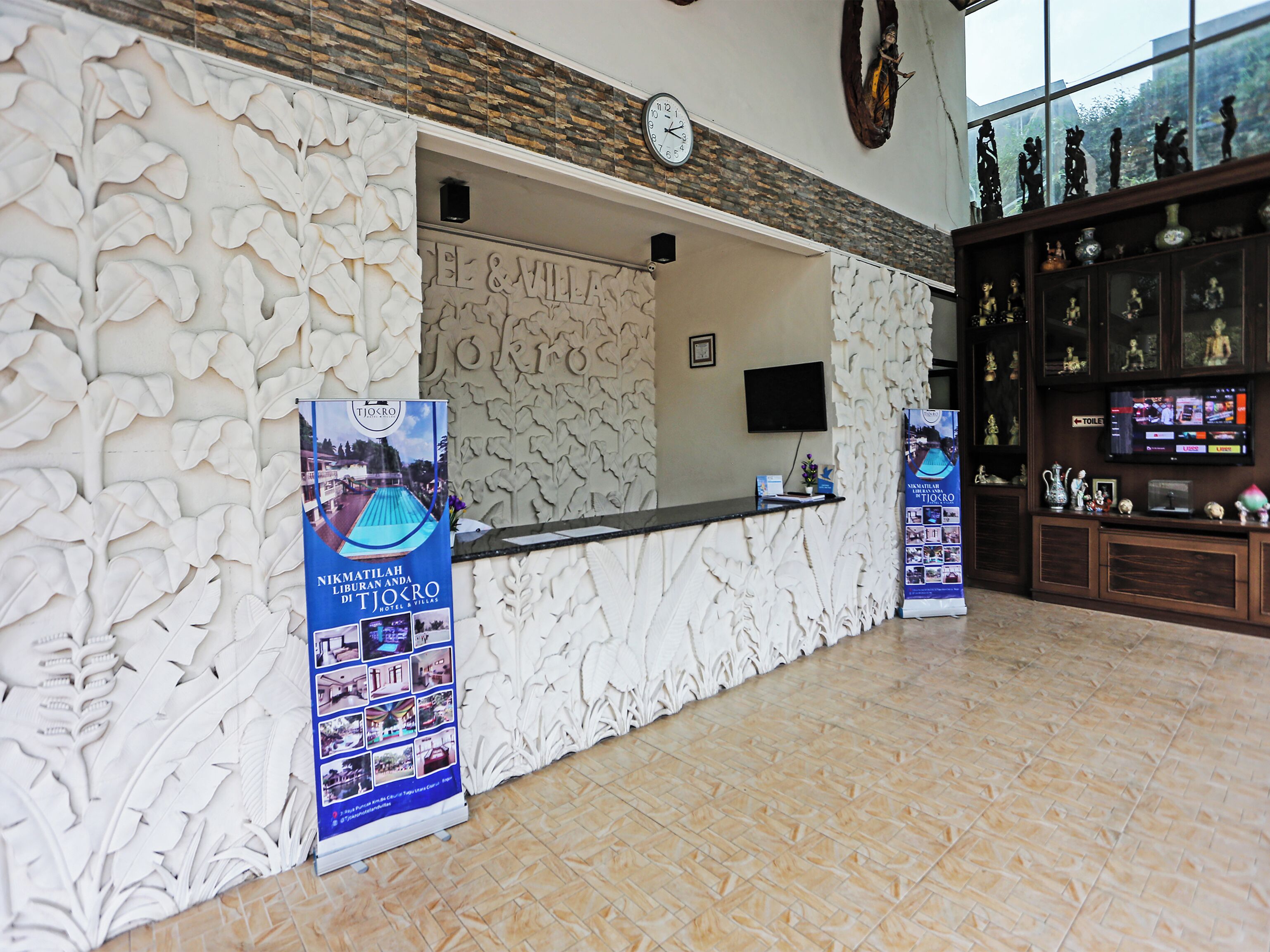 A reception area with a stone wall, a clock, a TV, and a display board.