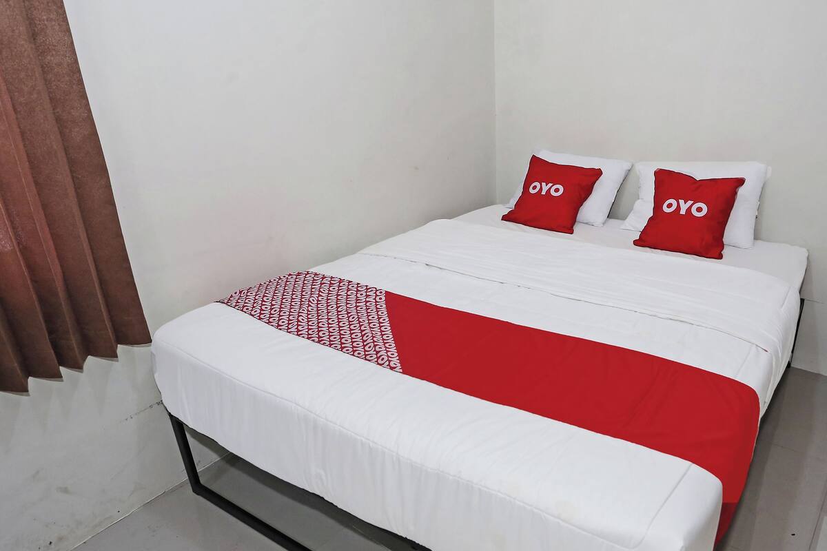 Een bed met witte beddengoed en rode accenten, waaronder kussens en een deken.