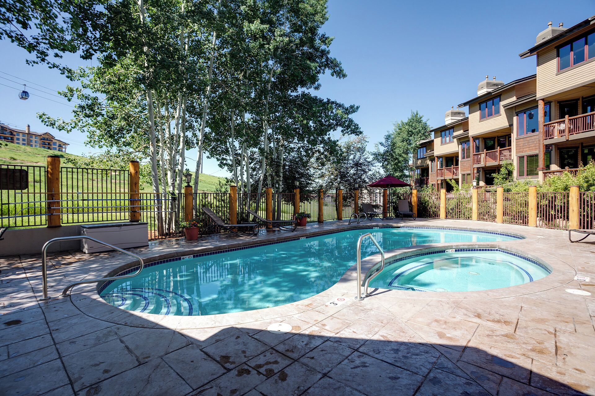 A swimming pool with a tiled deck, surrounded by a fence and trees.