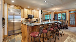 A kitchen with wooden cabinets, stainless steel appliances, a large island with bar stools, and a view through large windows.