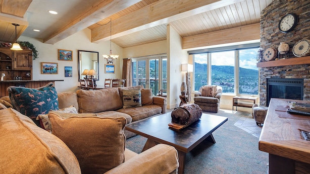 Un salon spacieux doté d’une cheminée, de poutres apparentes en bois et d’une grande fenêtre offrant une vue sur les montagnes.