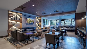 Un hall d’hôtel moderne doté d’une cheminée, de sièges confortables, d’un bar et de grandes fenêtres offrant une vue sur l’extérieur.