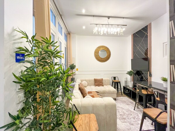 A modern living room with a sofa, a coffee table, and a TV. There is a plant in the corner and a sign indicating WiFi availability.