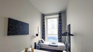 A small, modern hotel room with a single bed, a bedside table, a wall-mounted TV, and a large window with patterned curtains. - Urban Flat 94 - Sublime 4BDR Flat Coco Chanel (París)