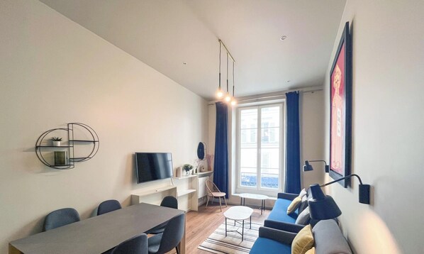 Ein modernes Wohnzimmer mit Essbereich, Fernseher und großem Fenster mit Vorhängen.