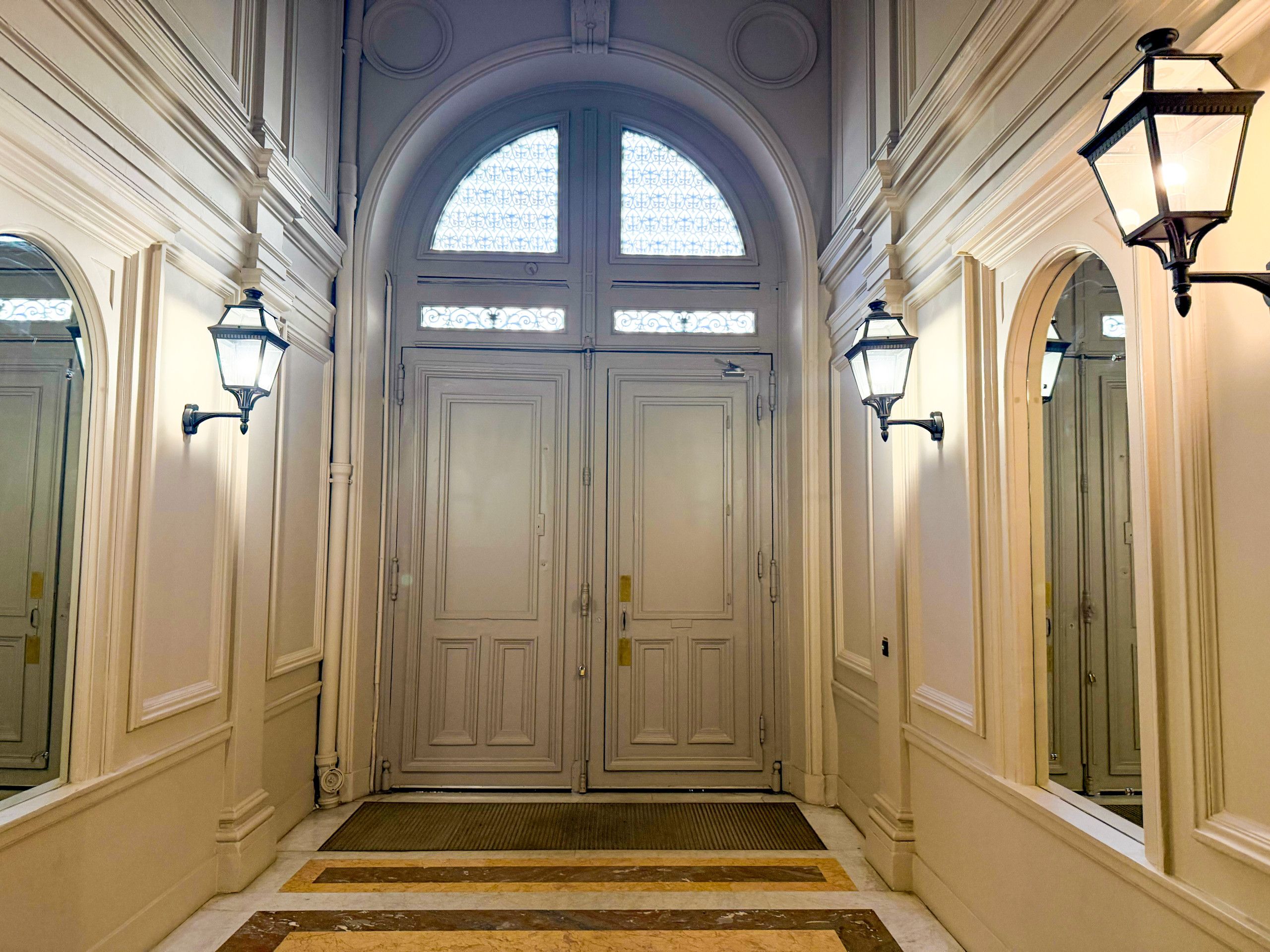A grand entrance with double doors, a patterned window above, and two wall-mounted lights.