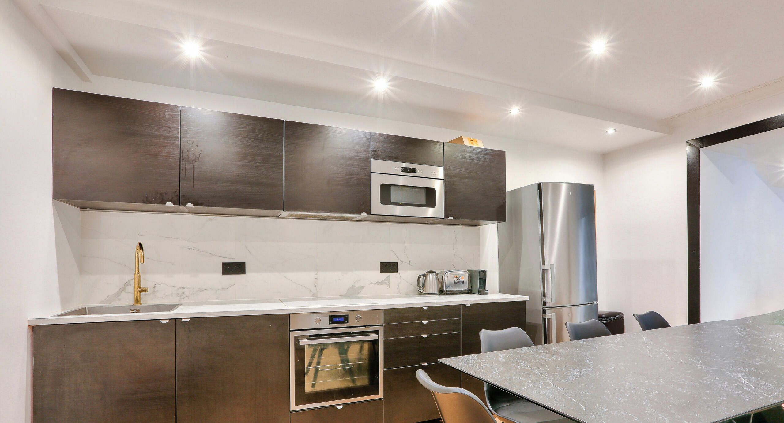 A modern kitchen with dark cabinetry, a built-in oven, a microwave, and a stainless steel refrigerator.