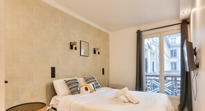 Une chambre d’hôtel avec un papier peint à motifs, un lit avec des oreillers, une fenêtre donnant sur des immeubles et un rideau.
