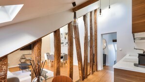 A modern kitchen with a wooden ceiling, a dining area with a round table and chairs, and a view of the living room through a glass partition. - Urban Flat  117 - Charming 3BDR Apartment in Paris (París)