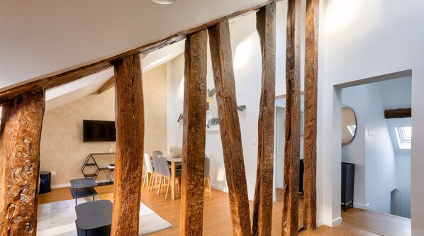Un interior moderno con vigas de madera a la vista, un comedor con una mesa redonda y sillas, y un televisor de pantalla plana montado en la pared.