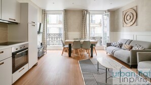 Un appartement moderne comprenant une cuisine, un coin repas et un salon. Il est doté d’une grande fenêtre, d’un canapé et d’une table basse.