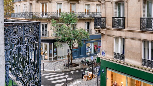 Une vue de rue avec un immeuble doté de nombreux balcons, une vitrine avec des mannequins et un passage piéton.