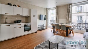 Une cuisine moderne avec des meubles blancs, un coin repas comprenant une table et des chaises, et une grande fenêtre agrémentée de rideaux.
