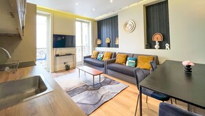 Ein modernes Wohnzimmer mit Sofa, Couchtisch und Esstisch. Es gibt eine Küchenzeile mit Spüle und einem Fernseher.