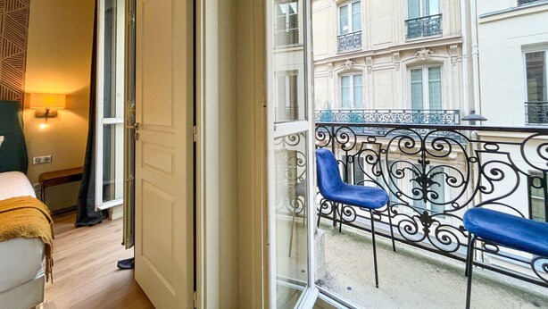 Ein Zimmer mit Balkon, einem Bett, einem Stuhl und einer Lampe.