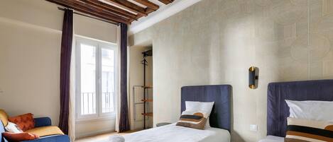 Une chambre d’hôtel avec deux lits, une fenêtre avec des rideaux, un plafond en bois et un papier peint à motifs.
