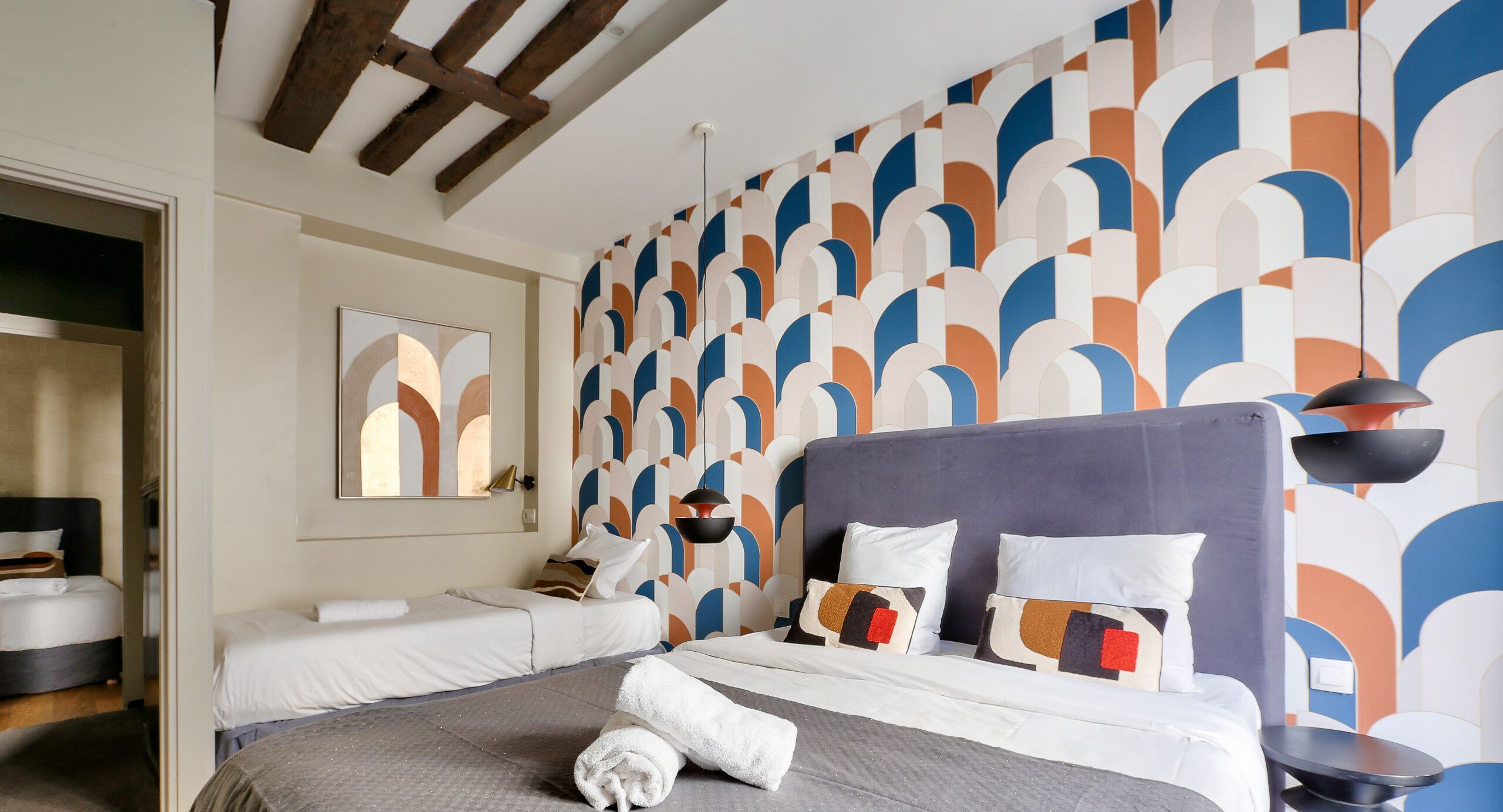 A hotel room with a large bed, two smaller beds, a mirror, and a patterned wall.