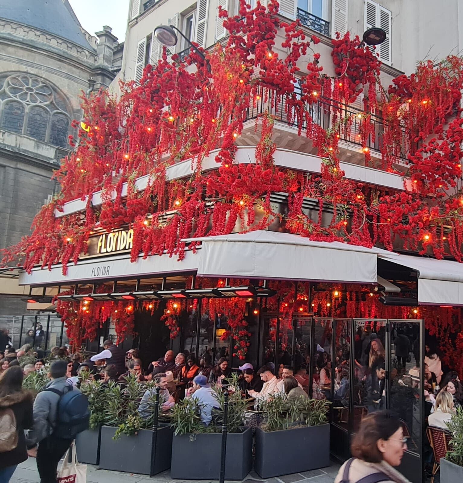 A restaurant with outdoor seating, covered by a white awning, and adorned with red floral decorations.