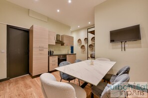 Une cuisine moderne avec des meubles en bois, une table à manger avec des chaises et un téléviseur à écran plat fixé au mur.