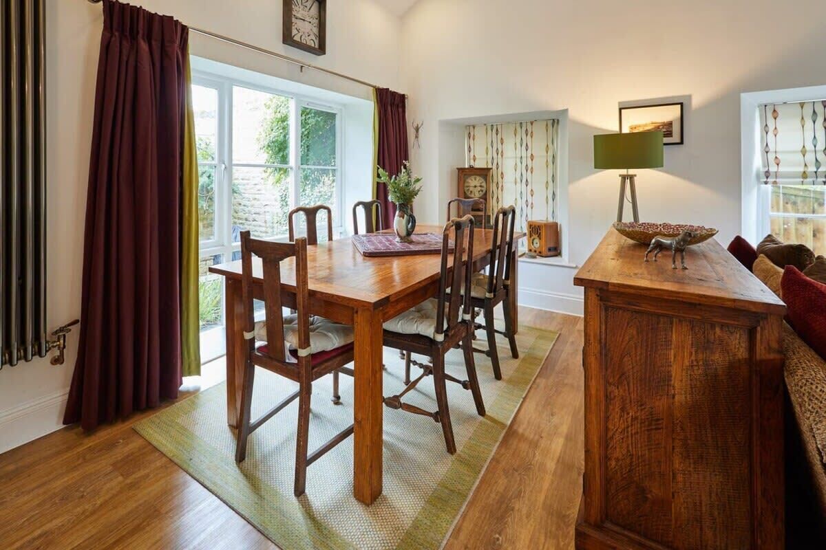 A dining area with a wooden table and chairs, a vase with flowers, a clock, and a lamp on a side table.