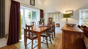 A dining area with a wooden table and chairs, a vase with flowers, a clock, and a lamp on a side table. - Host & Stay | River View Cottage (Barnard Castle)