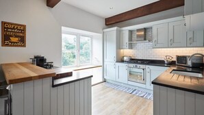 A modern kitchen with white cabinets, a wooden countertop, and a coffee-themed sign. - Host & Stay | River View Cottage (Barnard Castle)